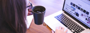 Woman reads latest news on laptop while drinking coffee